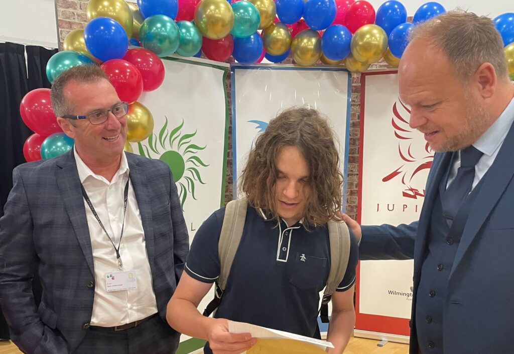 A student opening their GCSE results alongside two members of staff.