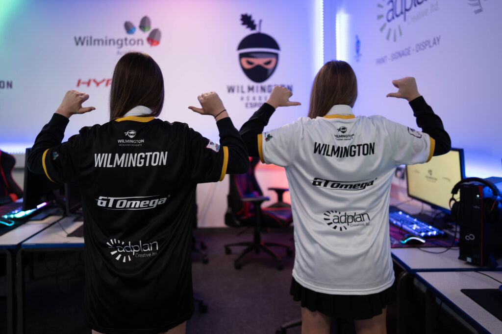 Two students with their backs to the camera, pointing at the backs of their Wilmington eSports t-shirts
