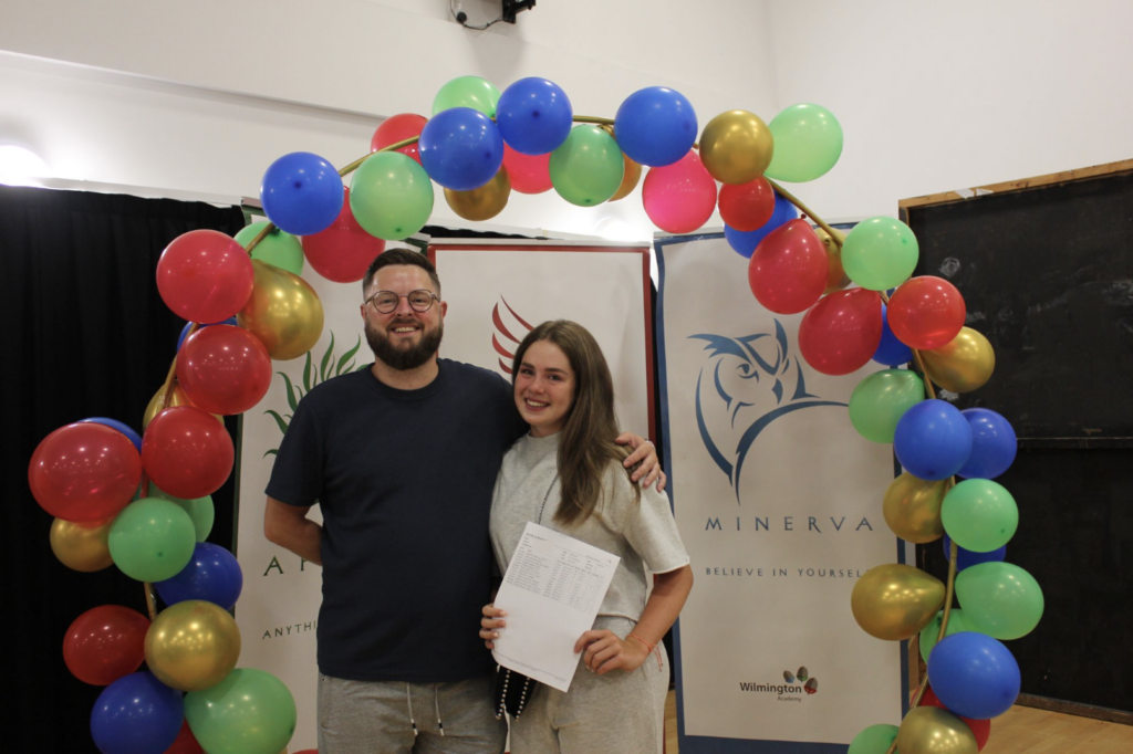 Students holding their results in front of a banner