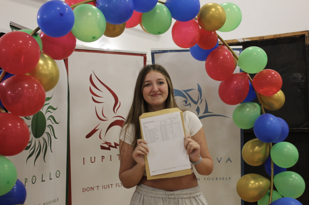 Student holding their results in front of a banner